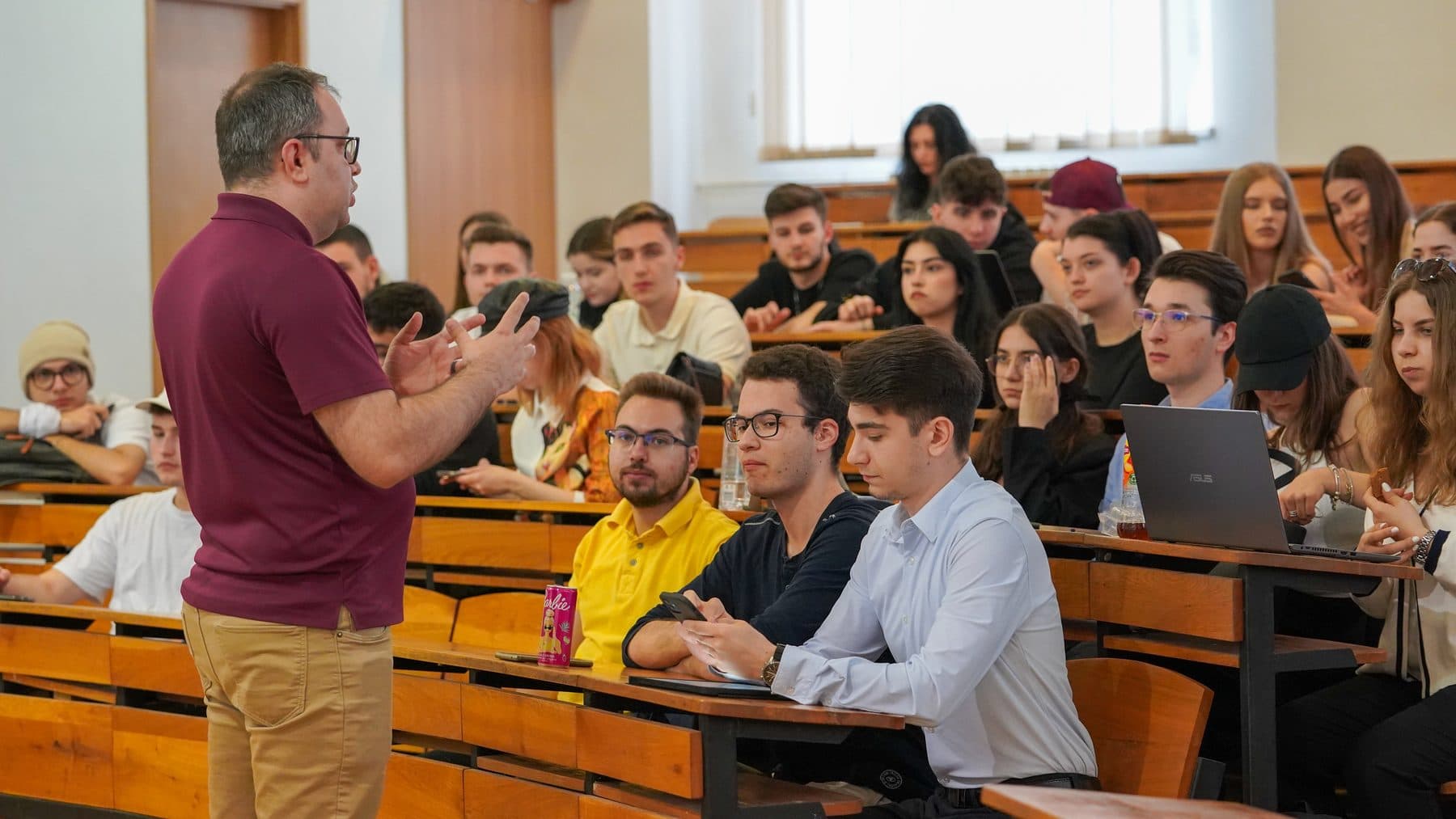 Invitat în tricou polo vișiniu discută cu studenți atenți într-un amfiteatru, la o sesiune LDM în facultate