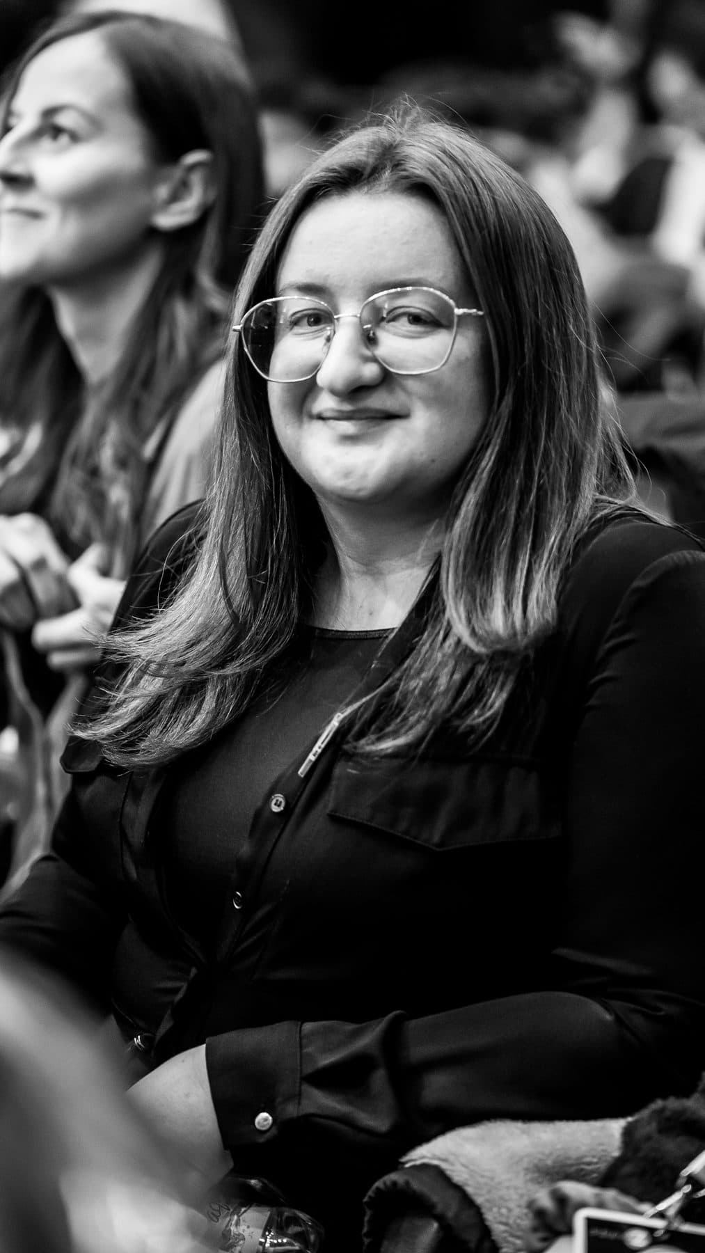 Portret alb-negru al unei tinere cu ochelari, zâmbind în public