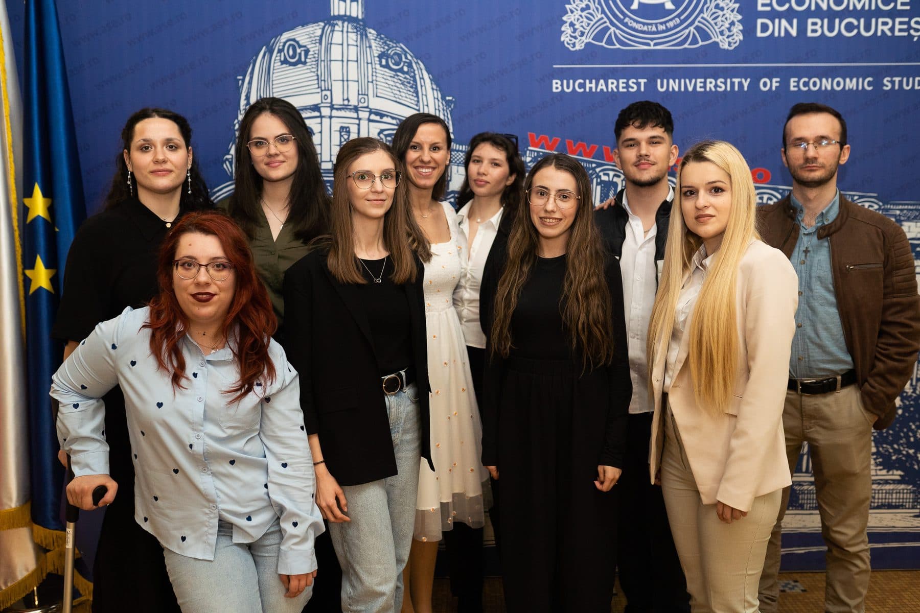 Echipa de organizare Liderii de Mâine pozează zâmbind în fața panoului albastru al ASE, la Ready for the Future