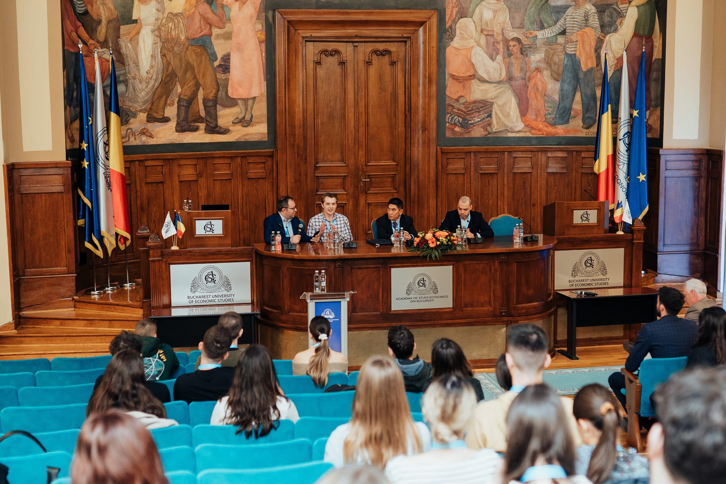 Panel de invitați pe scena aulei ASE, sub pictura murală, văzut din spatele sălii pline la Ready for the Future 2024