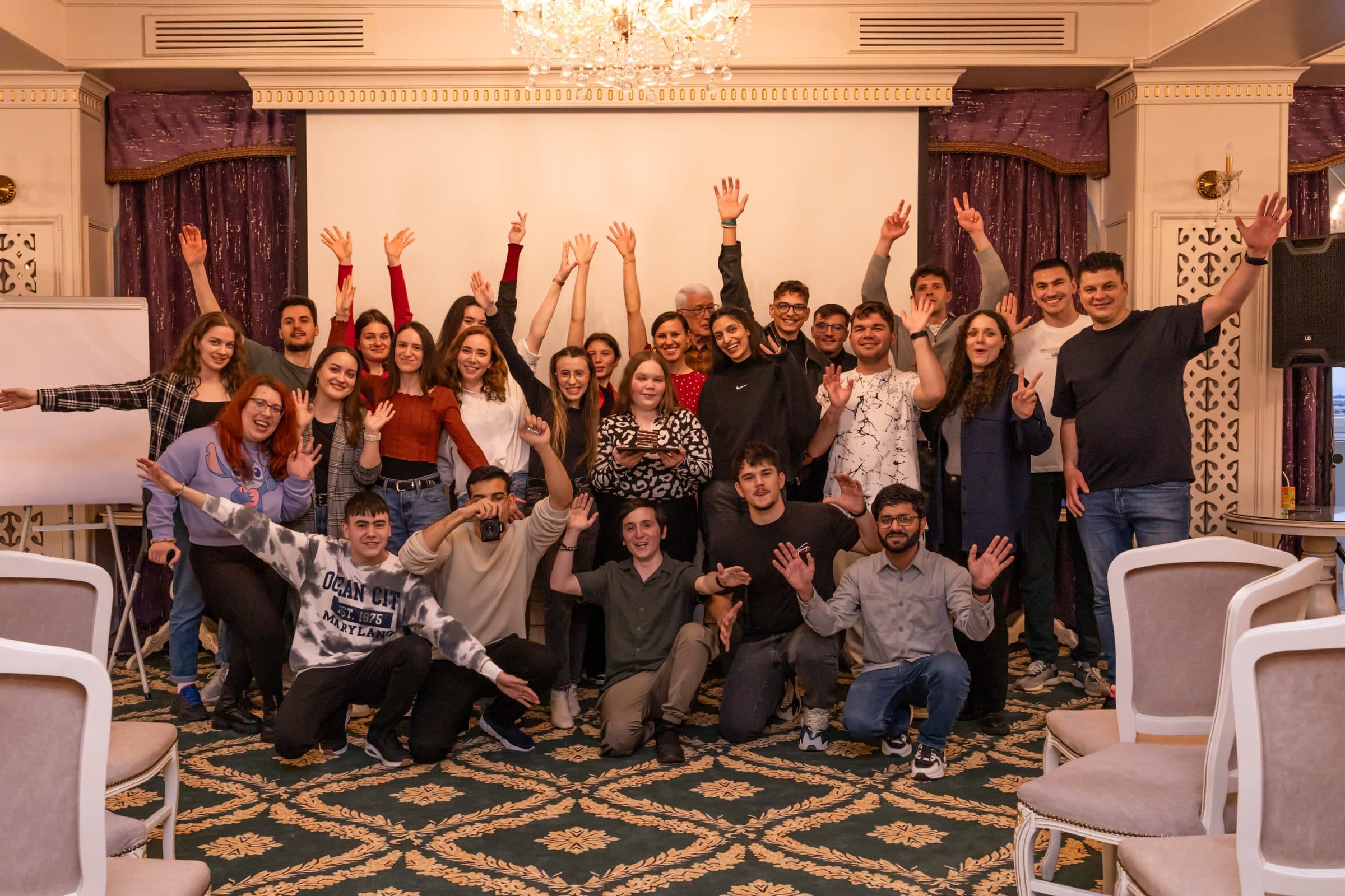Grup de studenți LDM bucuroși, cu mâinile ridicate și primul rând în genunchi, la teambuildingul din aprilie 2025