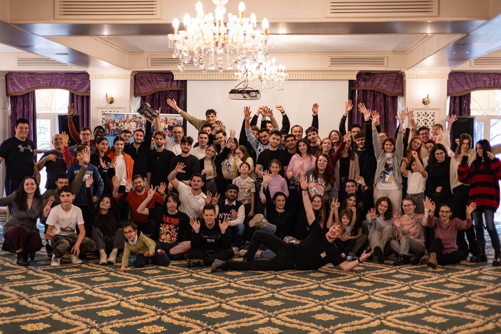 Peste 80 de studenți Liderii de Mâine cu brațele ridicate, într-o sală cu candelabre, la teambuildingul din noiembrie 2025