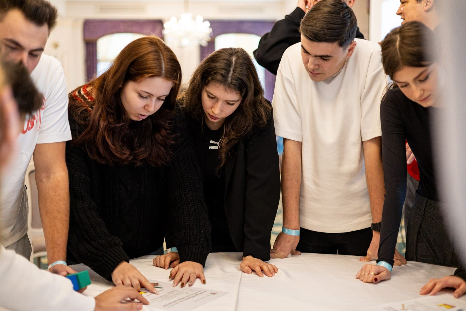 Cinci studenți aplecați peste o masă rezolvă împreună o provocare de echipă la teambuilding