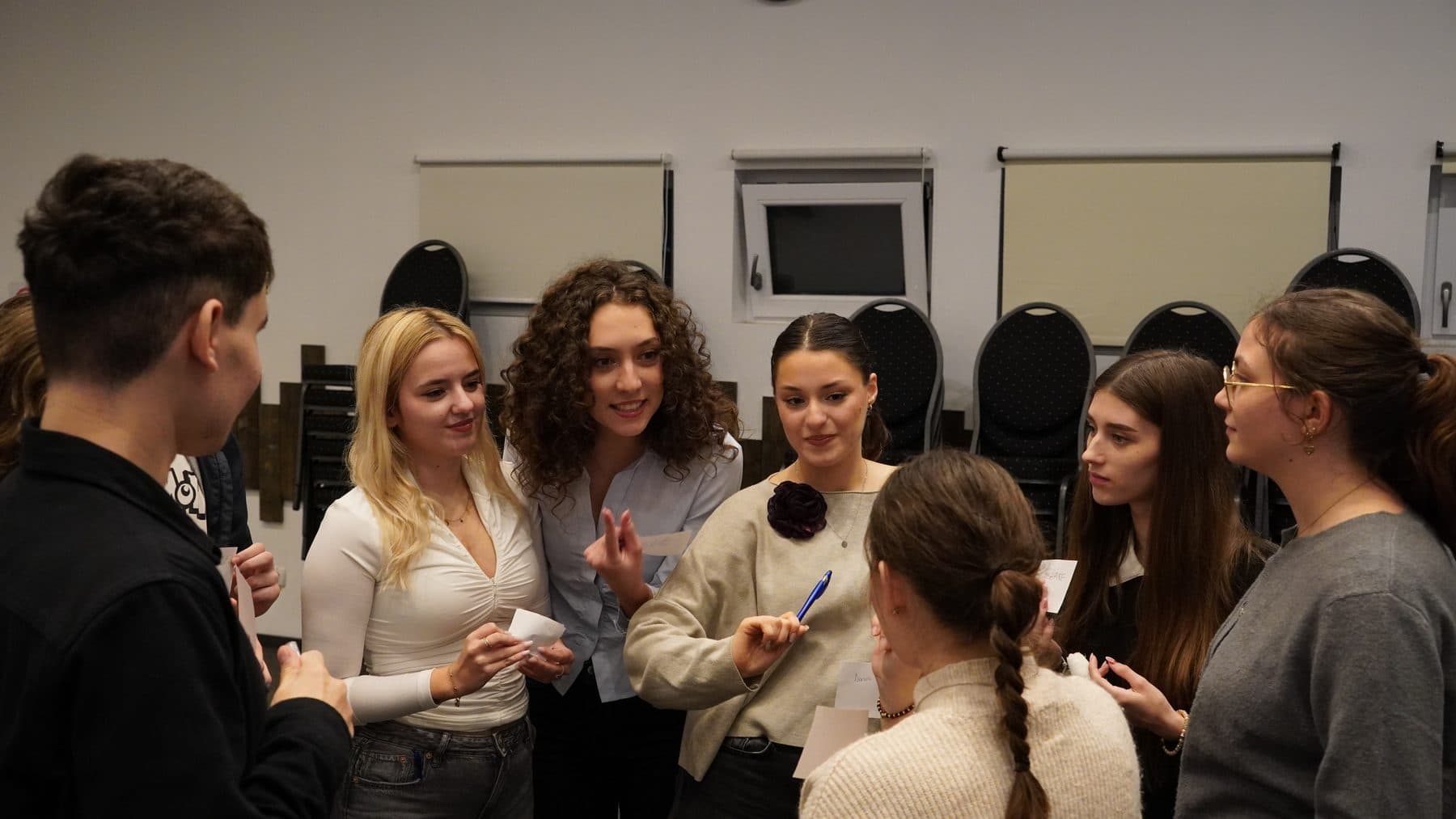 Studente adunate în cerc, zâmbind și discutând cu bilețele în mână în timpul unui exercițiu