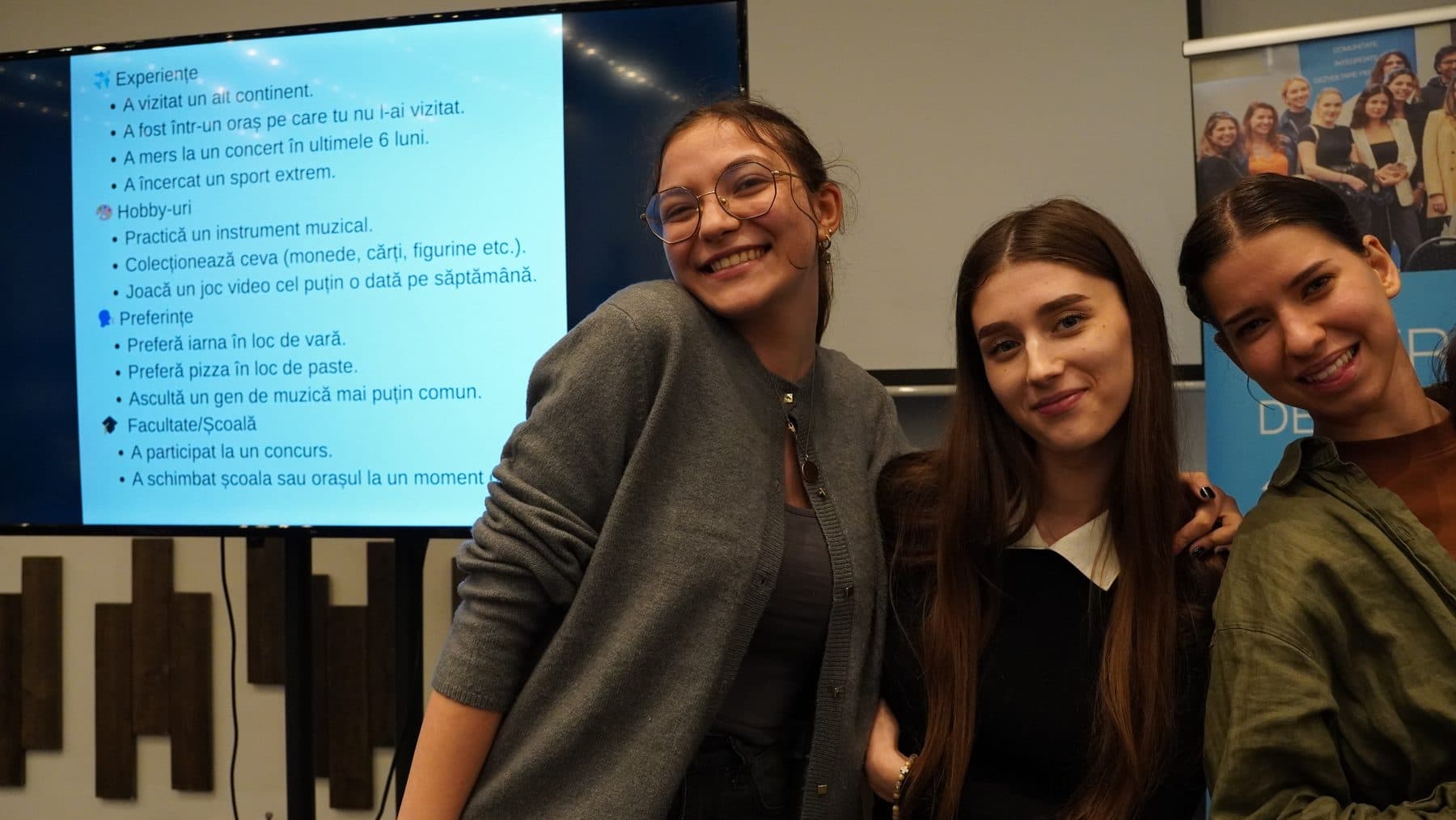 Trei studente îmbrățișate zâmbesc spre cameră la întâlnirea de marți